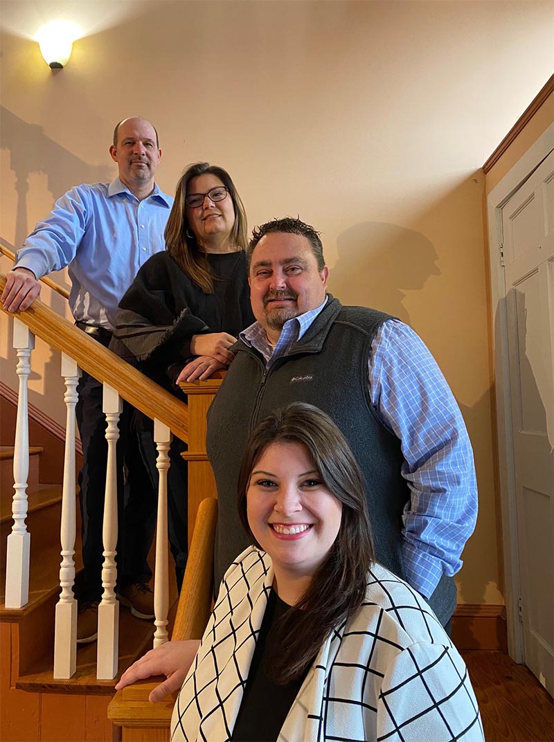 Homepage - Hunt Insurance Agency Team Smiling and -Posing for a Photo as They Stand on a Wooden Staircase